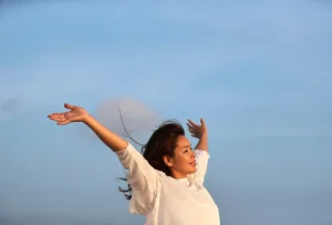 Happy woman with arms in the air feeling the breeze and a beautiful blue sky